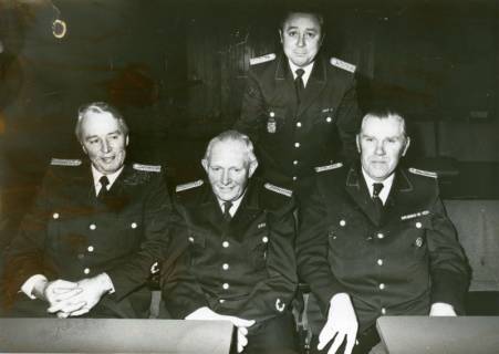 ARH Slg. Bartling 3319, Gruppenbild mit vier geehrten Feuerwehrleuten, drei sitzend, einer dahinter stehend, Neustadt a. Rbge., um 1975