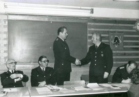 ARH Slg. Bartling 3322, Fritz Steege gratuliert dem Heinrich Schaper per Handschlag, beide stehend, im Lehrsaal; daneben sitzend: Grosse und Georg Meyer (l.) und Kreisbrandmeister Horst Dempewolf (r.), Wunstorf, um 1975