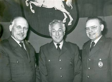 ARH Slg. Bartling 3358, Drei Polizisten nebeneinander vor der niedersächsischen Landesflagge an der Wand, Neustadt a. Rbge., um 1975