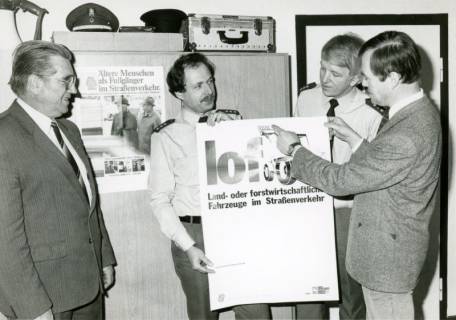 ARH Slg. Bartling 3380, Zwei Zivilisten bei der Überreichung eines Plakates der Verkehrswacht mit dem Titel "lof - Land- und forstwirtschaftliche Fahrzeuge im Straßenverkehr" an zwei Polizisten, Neustadt a. Rbge., um 1974