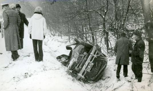 ARH Slg. Bartling 3392, Im Schnee von der B 6 abgekommener und in den Straßengraben gerutschter, auf der Seite liegender VW-Käfer, Blick von hinten auf den PKW und auf einige Betrachter, 1970