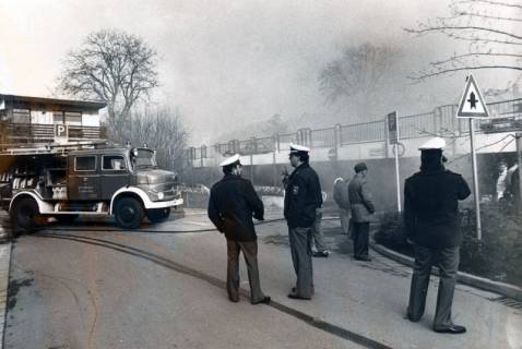 ARH Slg. Bartling 3436, Drei Polizisten vor der Einfahrt zur Parkpalette, durch die dichter Rauch quillt; links ein Löschfahrzeug der Feuerwehr mit offenem Seitenteil, Neustadt a. Rbge., um 1975