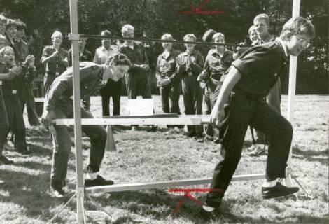 ARH Slg. Bartling 3438, Auf einer Wiese tragen zwei Mitglieder der Jugendfeuerwehr unter dem Beifall der umstehenden Kollegen eine Leiter unter ein Joch, Neustadt a. Rbge., um 1975