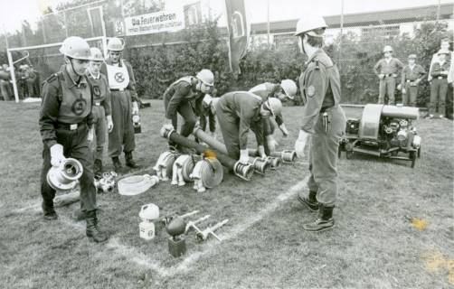 ARH Slg. Bartling 3439, Auf einem Rasen-Fußballplatz bereiten Mitglieder der Jugendfeuerwehr einige Wasserschläuche und Spritzen für eine Löschübung vor, Neustadt a. Rbge., 1975