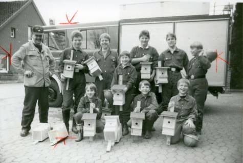 ARH Slg. Bartling 3440, Gruppenbild von Mitgliedern der Jugendfeuerwehr mit Ausbilder auf einem gepflasterten Platz vor einem Feuerwehrwagen, alle mit einem selbst gebauten Nistkasten in der Hand, Neustadt a. Rbge., um 1975