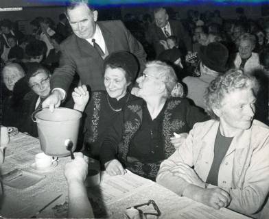 ARH Slg. Bartling 3454, Pastor Helmut Niemeyer (in Zivil) eine Wahlurne (Wassereimer) über den Tisch reichend bei einem Seniorennachmittag mit Kaffee, Kuchen und Gesang, Neustadt a. Rbge., 1972