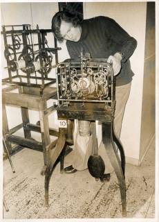 ARH Slg. Bartling 3482, Junger Mann in einer Uhrensammlung hinter dem Laufwerk einer Turmuhr stehend und das Laufwerk reparierend, daneben ein weiteres Uhrwerk, Neustadt a. Rbge., um 1972