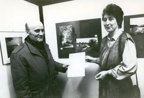 ARH Slg. Bartling 3655, Überreichung einer Urkunde an einen Mann durch die Bürgermeisterin Ursula Baldauf (CDU) vor Stellwänden mit Landschaftsfotografien, Neustadt a. Rbge., um 1975