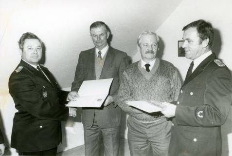 ARH Slg. Bartling 3680, Ehrung von zwei älteren Mitgliedern der Otternhagener Feuerwehr (in Zivilkleidung) und Überreichung einer Urkunde in einem Dachzimmer durch Stadtbrandmeister Horst Liem (li.) und N. N., Otternhagen, um 1985