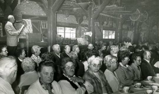 ARH Slg. Bartling 3700, Zahlreiche ältere Leute in der Zehntscheune, Blick über zwei Reihen einer Kaffeetafel, links ein Redner am Mikrofon, Mandelsloh, 1986
