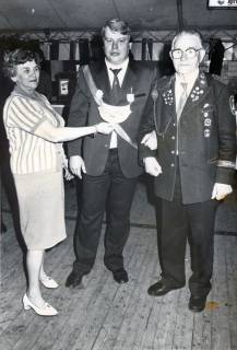 ARH Slg. Bartling 3736, Jüngerer Schütze in Uniform mit Königsplakette auf der Brust (Mitte) im Festzelt, links eine Frau, die mit ihrer Linken die Königsplakette hält, rechts ein Schütze in mit Orden übersätem Uniformjackett, das mit vielen Ehrenzeichen geschmückt ist, Schneere, um 1980