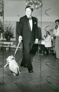 ARH Slg. Bartling 3767, Mann im Smoking beim Spaziergang durch den geschmückten Festsaal des FZZ mit einem Glücks-Schwein an der Leine, Neustadt a. Rbge., 1975