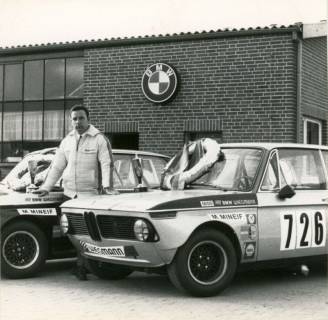 ARH Slg. Bartling 3871, Manfred Mineif, Rennfahrer aus Bordenau, vor einer Werkstatt mit BMW-Logo über der Eingangstür und zwischen zwei für den Motorsport getunten BMW 1800, auf der Motorhaube des ersten ein Siegerkranz, auf der des zweiten ein Pokal, Bordenau, 1969