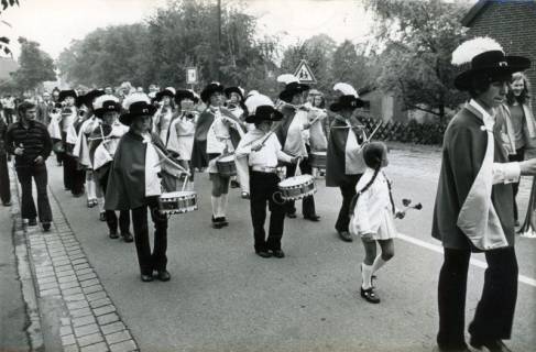 ARH Slg. Bartling 3903, Schützenumzug, Fanfarenzug (mit schwarzem Federhut) in Marschformation auf einer Straße unter der Stabführung einer Frau des Schützenverein, Bordenau, um 1975