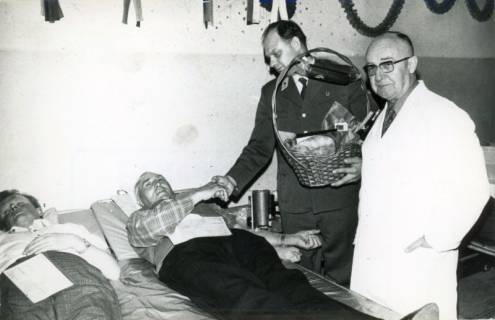 ARH Slg. Bartling 3944, Überreichung eines Präsentkorbs an einen verdienten Blutspender durch den Vorsitzenden der DRK- Ortsgruppe Bordenau Friedhelm Löffelholz und einen Arzt nach der Blutspende am Ruhebett, Bordenau, 1971