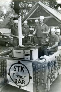 ARH Slg. Bartling 4080, Männer aus dem STK Eilvese mit älterem Küchenherd und Pfanne auf einem Wagen (mit der Aufschrift "STK Turner BAR") beim Erntefestumzug, Eilvese, um 1980