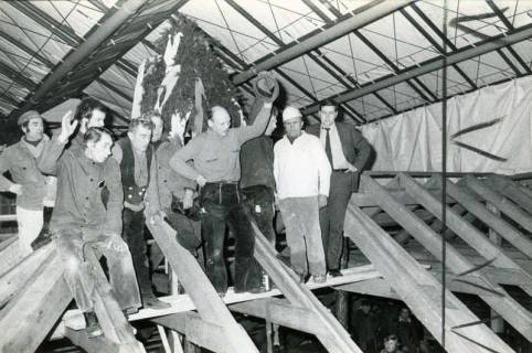 ARH Slg. Bartling 4100, Richtfest mit acht Zimmerleuten und dem Eilveser Firmenchef Friedrich Duensing (r.) auf dem Dachstuhl unter dem Richtkranz, über dem Dachsstuhl ein größeres Zeltdach, Eilvese, 1974