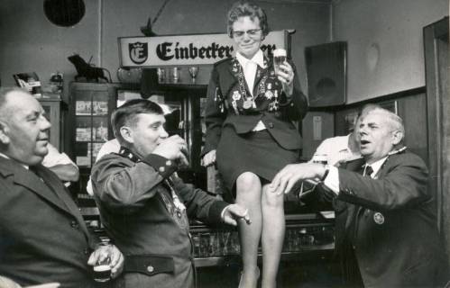 ARH Slg. Bartling 4167, Der Vorsitzende des Schützenvereins Empede-Himmelreich Erwin Brase (r.) und zwei weitere Männer lassen die Schützenkönigin, die auf dem Tresen einer Gastwirtschaft sitzt, hochleben, Empede, 1971