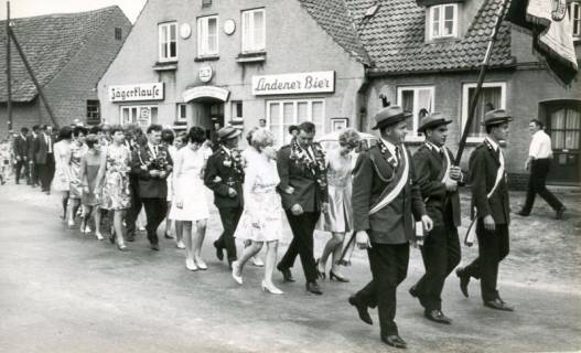ARH Slg. Bartling 4169, Die Schützenkönige ziehen, begleitet von Hofdamen und verfolgt vom Volk, vorweg die Schützenvereinsfahne in geordnetem Umzug durch die Straßen, vorbei an der Jägerklause, Empede, um 1970
