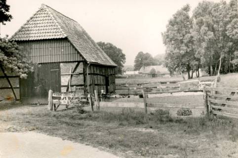 ARH Slg. Bartling 4227, Schafstall am Hagener Bach, Blick zwischen den Giebel des Fachwerkbaus (l.) und einen bewaldeten Hügel über den Weidezaun auf einen Bauernhof, Hagen, um 1975