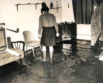 ARH Slg. Bartling 4243, Überschwemmung im Neubaugebiet, Frau mit Stiefeln geht durch das Wasser in ihrem Wohnzimmer, Helstorf, 1970
