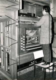 ARH Slg. Bartling 4266, Orgelbauer auf dem Stuhl stehend bei Reparaturarbeiten am geöffneten Spielschrank in der Kirche, Helstorf, 1972