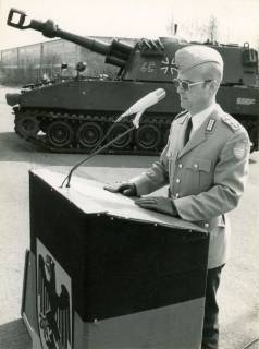 ARH Slg. Bartling 4304, Bataillonskommandeur Oberstleutnant Stammel in Dienstuniform bei einer Ansprache an das Bataillon am Rednerpult, das mit der deutschen Nationalflagge geschmückt ist, auf dem Exerzierplatz der Kaserne, Luttmersen, 1990