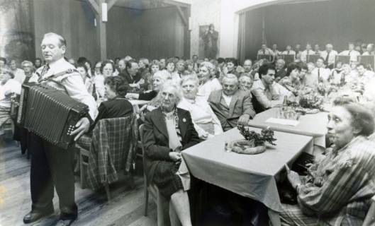 ARH Slg. Bartling 4427, Gut gesuchte Versammlung im Saal des Gasthauses Küster, Blick diagonal über die Kaffeetische, rechts die Bühne mit einer Musikband, links der Auftritt eines Akkordeonspielers, Mandelsloh, um 1980