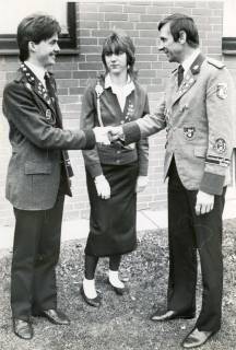 ARH Slg. Bartling 4476, Begrüßung von zwei Schützenvertretern in Uniform per Handschlag, dazwischen eine Schützin mit Schießschnur und mehreren Abzeichen an der Weste, Mariensee, um 1980