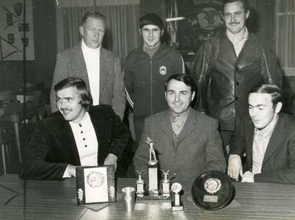 ARH Slg. Bartling 4487, Sechs erfolgreiche Schützen des Schützenvereins, und zwar drei am Tisch sitzend (darunter in der Mitte: Rainer Rebe), drei dahinter stehend, auf dem Tisch die Trophäen, Mariensee, 1973