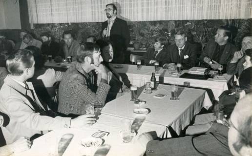 ARH Slg. Bartling 4574, Vortrag des Regierungsrats Jochen Hagemann (stehend) vor am Tisch sitzenden Männern in der Neuen Moorhütte, Mardorf, um 1975