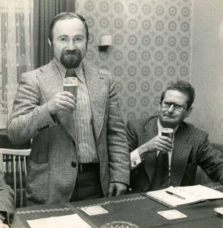 ARH Slg. Bartling 4581, Ortsratsvorsitzender von Laderholz Heiner Meier (l.), hinter einem Tisch stehend und Stadtdirektor Felix Rohde, sitzend, beim Zuprosten mit einem Glas Bier, Laderholz, um 1975