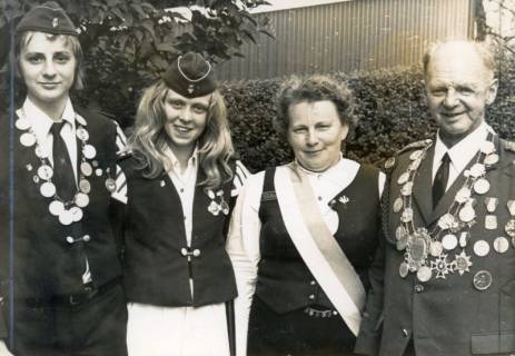 ARH Slg. Bartling 4582, Drei Schützenköniginnen und ein Schützenkönig nebeneinander stehend vor einer Hecke, Lichtenhorst, um 1975