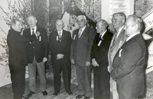 ARH Slg. Bartling 4607, Ehrung von sechs nebeneinander stehenden Mitgliedern des Kyffhäuserbundes, Ortsgruppe Mardorf (?), durch N. N. (l.) vor einer Wand mit Birken-Fototapete und zwei Vereinsfahnen, um 1986