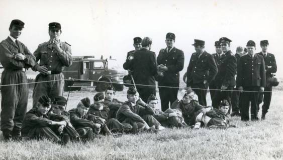 ARH Slg. Bartling 4654, Uniformierte Feuerwehrleute in der Pause beim Feuerwehrfest, die Jugend sitzend im Gras, die Erwachsenen stehend dahinter, im Hintergrund ein Löschfahrzeug (LF 16/25), Metel, 1970