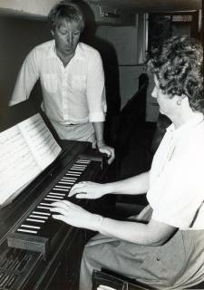 ARH Slg. Bartling 4686, Junge Frau sitzend beim Spiel auf einer elektronischen Orgel,  am Ende stehend und zuhörend ein junger Mann, Niedernstöcken?, um 1980