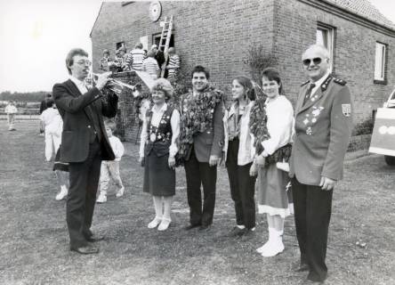 ARH Slg. Bartling 4711, Annageln der Schützenscheibe am Haus des 1. Vorsitzenden Manfred Kettner (r.) beim Schützenfest, auf dem Rasen im Vorgarten nebeneinander stehend die Königinnen und Könige, links ein Trompeter, Nöpke, um 1975