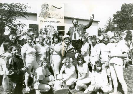 ARH Slg. Bartling 4712, Annageln der Schützenscheibe am Haus des N. Schwarz beim Schützenfest, auf dem Rasen vor dem Wirtschaftgebäude aufgestellt der winkende Schützenkönig inmitten von zahlreichen jüngeren Frauen in Weiß maskiert mit Schweinenase, Nöpke, um 1975