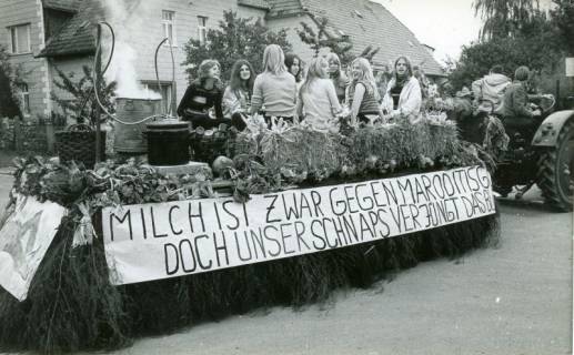 ARH Slg. Bartling 4718, Jugendliche Frauen auf einem geschmückten Wagen sitzend mit einfacher Destillieranlage, Wagenbeschriftung: "Milch ist zwar gegen Maroditis gut, doch unser Schnaps verjüngt das Blut" beim Erntefestumzug, Nöpke, 1971