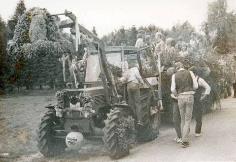 ARH Slg. Bartling 4721, Fendt-Traktor mit Frontlader, an dem die Erntekrone hängt von vorn, auf dem geschmückten Anhänger zahlreiche junge Leute beim Erntefestumzug, Nöpke, 1985