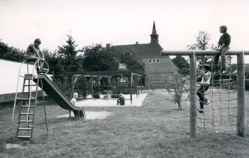 ARH Slg. Bartling 4743, Blick über die Spielgeräte (Rutsche und Klettergerüst) des Kinderspielplatzes auf die benachbarte alte Schule mit Dachreiter (2. Ex.), Nöpke, um 1975