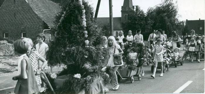 ARH Slg. Bartling 4782, Kinder ziehen eine Erntekrone, die mit Heidekraut und Blumen geschmückt ist, auf einem Bollerwagen, gefolgt von zahlreichen anderen Kindern beim Erntefestumzug, Otternhagen, 1971
