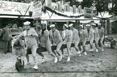 ARH Slg. Bartling 4849, Neun Personen in geringelter Badekleidung auf einem Riesenfahrrad vor den Verkaufsbuden beim Heideblütenfest, Otternhagen, 1972
