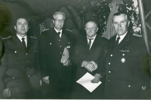 ARH Slg. Bartling 4918, Überreichung von Ehrenurkunden an drei nebeneinander stehende ältere Mitglieder durch Ortsbrandmeister Wilhelm Oehlerking (r.), Scharrel, um 1975