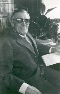 ARH Slg. Bartling 4930, Unbekannter älterer Herr aus Scharrel (?) mit getönter Brille, mit Anzug bekleidet, in wohnlicher Umgebung sitzend, mit einem Schriftstück in der Linken, Scharrel, um 1980
