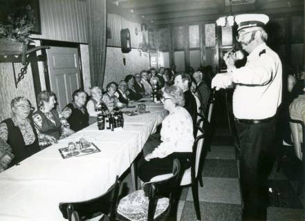 ARH Slg. Bartling 4960, Altennachmittag im Wirtshaussaal, die Senioren an einem langen Tisch sitzend und schunkelnd, ein Alleinunterhalter mit Mikrofon rechts daneben stehend, Suttorf, um 1975