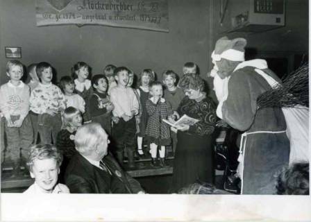 ARH Slg. Bartling 619, Weihnachtsfeier für Vorschulkinder, Gruppe von Kindern auf einer Bühne, davor rechts der Weihnachtsmann, über den Kindern an der Wand ein Brett mit den Daten der Baugeschichte des Vereinsheims, Stöckendrebber, um 1978