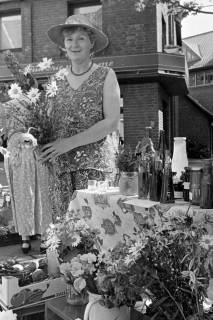 ARH Slg. Weber 02-003/0005, Eine Frau mit einem Blumenstrauß in der Hand steht an einem Wochenmarkt-Stand? mit unterschiedlichen Waren, zwischen 1980/1990