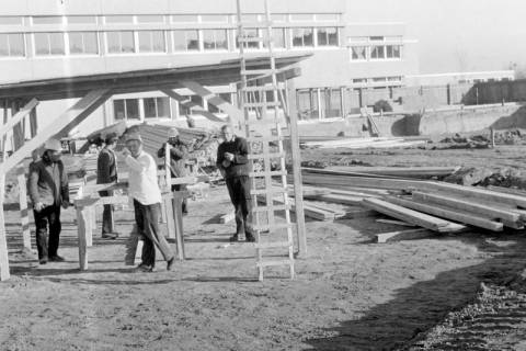 ARH Slg. Weber 02-021/0002, Bauarbeiter stehen auf einer Baustelle unter einem Baugerüst vor der Haupt- und Realschule, Gehrden, zwischen 1980/1990