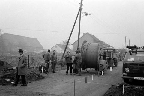 ARH Slg. Weber 02-031/0014, Männer verlegen neben einer Straße Kabel mithilfe einer Kabeltrommel, zwischen 1970/1980